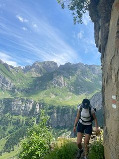 a woman hiking up the side of a mountain with green mountains in the back ground