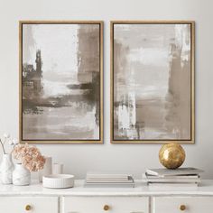 two abstract paintings hang on the wall above a white dresser with vases and books