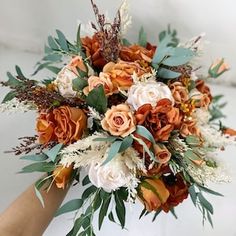 a bridal bouquet with orange, white and green flowers is held by someone's hand