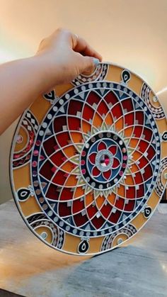 a hand holding a decorative plate on top of a table