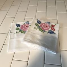 two white sheets with pink and blue flowers on them sitting on a tiled floor next to each other