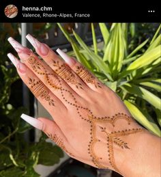 a woman's hand with henna on it and some plants in the background