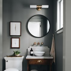 a white toilet sitting next to a bathroom sink under a round mirror on a wall