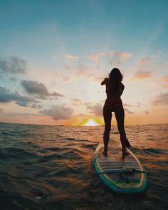 a woman is standing on a surfboard in the ocean at sunset or dawn with her arms outstretched