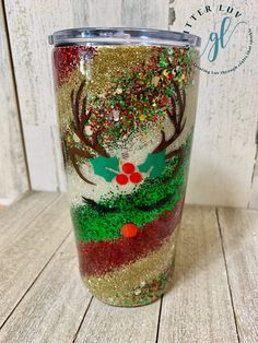 a christmas themed tumbler with glitter and reindeer antlers on it, sitting on a wooden table