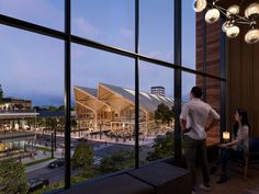 two people are looking out the window at an outdoor plaza and shopping center in the evening