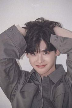 a young man with black hair and grey shirt holding his hands to his head while posing for the camera