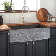 a kitchen with black cabinets and marble counter tops, wooden cutting board on the sink