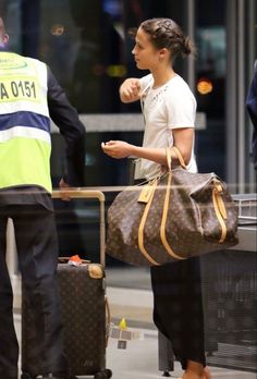 a woman standing next to a man holding a brown bag and luggage in her hand