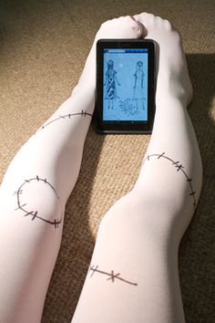 a person wearing tights with barbed wire on their legs, looking at a cell phone