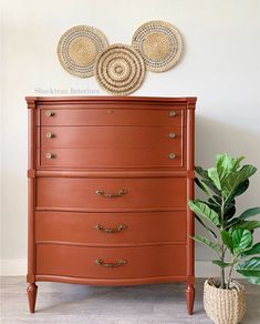 an orange dresser next to a potted plant and two wicker circles on the wall