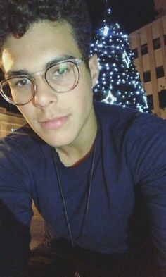 a young man wearing glasses is taking a selfie in front of a christmas tree