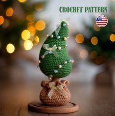 a small crocheted christmas tree sitting on top of a wooden stand with lights in the background