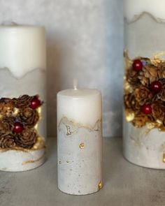 three white candles decorated with pine cones and berries