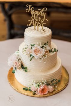 a white wedding cake with flowers and the words happily wed me on top is sitting on a gold plate