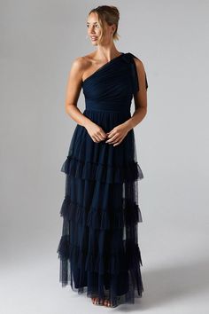 a woman wearing a black dress with one shoulder and tiered layers on the bottom