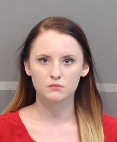 a woman with long blonde hair wearing a red shirt is looking at the camera while standing in front of a gray wall