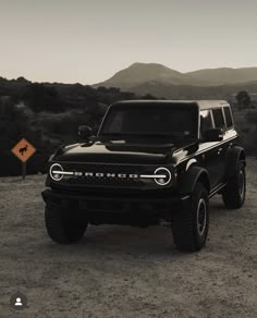 a black truck parked in the middle of a dirt field with mountains in the background