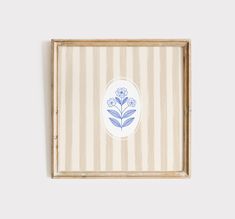 a blue and white flower on a striped background in a wooden frame hanging on the wall