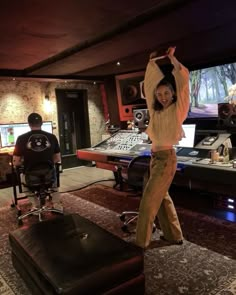 a woman standing in front of a mixing desk with headphones on and arms up