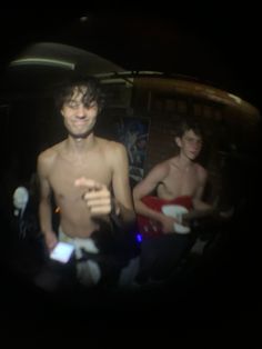 two shirtless men standing next to each other in front of a mirror with lights on