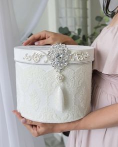 a woman holding a white box with a crystal brooch on it