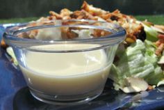 a blue plate topped with salad and dressing next to a glass bowl filled with dressing