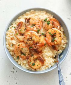 a bowl filled with shrimp and rice on top of a white counter next to a fork