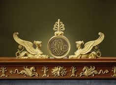 an ornate gold clock with two lions on it's sides and a monogram in the middle