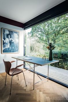 a room with a table, chair and large window looking out onto the trees outside