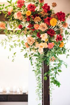 a tall vase filled with lots of flowers on top of a wooden table covered in greenery