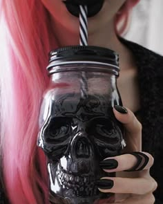 a woman with pink hair holding a mason jar filled with black liquid and a skull