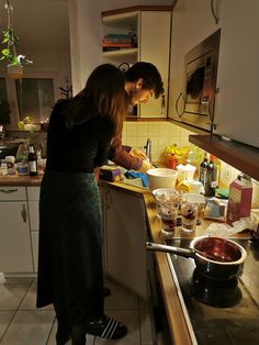 two people in a kitchen preparing food on the stove top and sink area, one woman is washing dishes while the other stands behind her