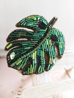 a brooch with green beads on it sitting on top of a wooden stand in front of a white wall