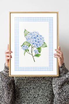 a woman is holding up a blue and white hydrangea print with green leaves