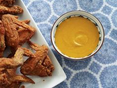 some fried food on a white plate next to a bowl of mustard and dipping sauce