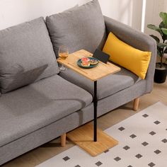 a gray couch with yellow pillows and a wooden tray on it next to a glass of wine