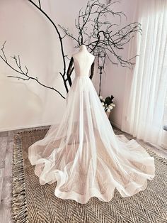 a wedding dress on display in front of a tree with no leaves and branches behind it