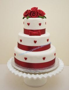 a three tiered wedding cake with red roses on top and hearts on the bottom