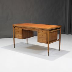 a wooden desk sitting on top of a white floor next to a gray wall and black curtain