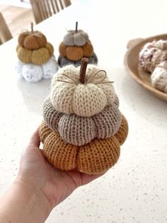 a hand holding a stack of knitted pumpkins on top of a white table