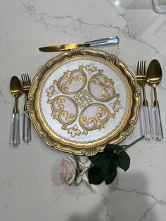 an ornately decorated gold plate with silverware and flowers on the countertop next to it