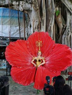 a woman in a red dress holding a large red flower next to a man with a camera