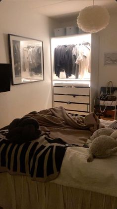 an unmade bed in a bedroom with clothes hanging on the wall