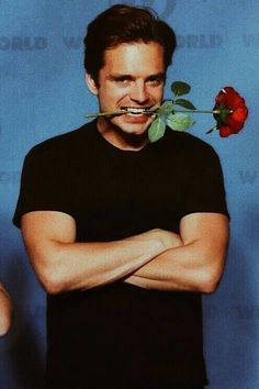 a man with a fake rose in his mouth standing next to a blue wall and looking at the camera