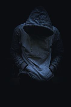 a person wearing a hoodie sitting in the dark with their hands on their knees