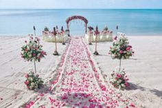 an outdoor wedding set up on the beach with pink flowers and white linens in the sand