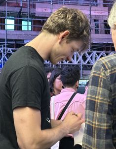 two men standing next to each other in front of a crowd looking at their cell phones