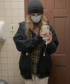 a woman wearing a face mask while taking a selfie in the bathroom with her cell phone