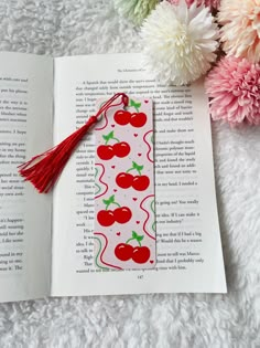 an open book with cherries and tassels on it, next to flowers